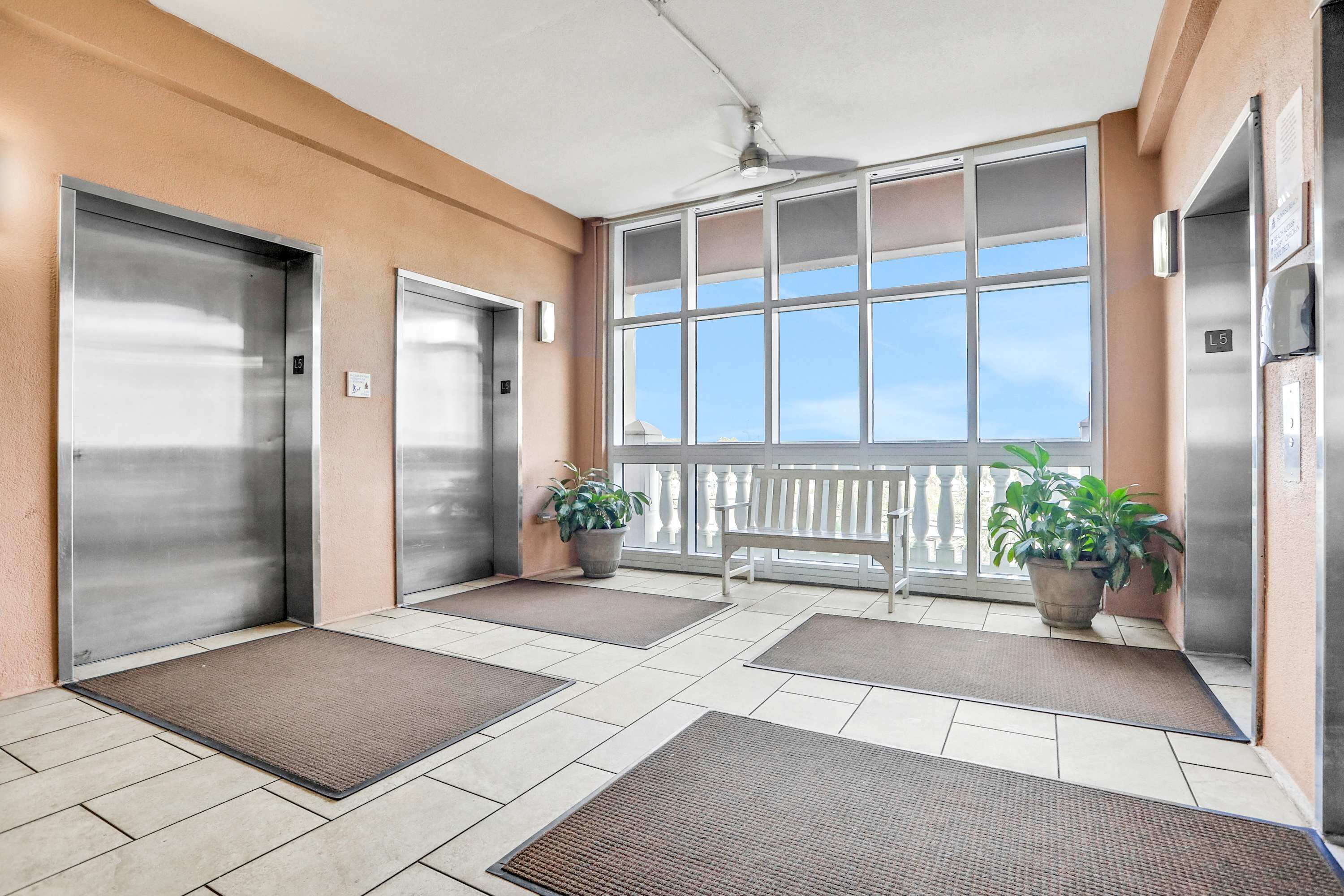 A hotel lobby with two elevators, a bench, and potted plants.