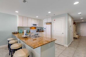 A modern kitchen with white cabinets, granite countertops, a built-in oven, and a stainless steel sink. - Spacious condo with breathtaking views & convenient location (Panama City Beach)