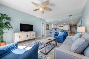 A modern living room with a flat-screen TV, a ceiling fan, and a large potted plant. - Spacious condo with breathtaking views & convenient location (Panama City Beach)