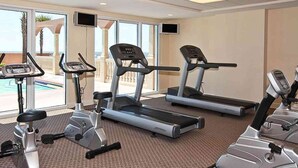 Un gimnasio con cintas de correr y bicicletas estáticas, ventanas amplias con vista a una piscina y palmeras.