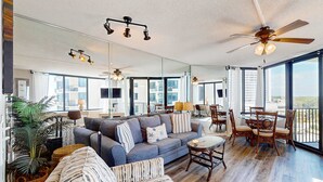 A spacious living area with a large sofa, a dining table with chairs, and a ceiling fan. - Beautiful beachfront condo with private balcony and shared pool (Panama City Beach)