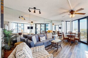 A spacious living area with a large sofa, a dining table with chairs, and a ceiling fan. - Beautiful beachfront condo with private balcony and shared pool (Panama City Beach)