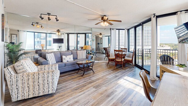 A spacious living room with a sofa, armchairs, a coffee table, and a dining area with chairs and a table. There is a ceiling fan and large windows providing natural light. - Beautiful beachfront condo with private balcony and shared pool (Panama City Beach)