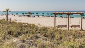 A beach with a wooden gazebo, lounge chairs, and umbrellas. - Beautiful beachfront condo with private balcony and shared pool (Panama City Beach)