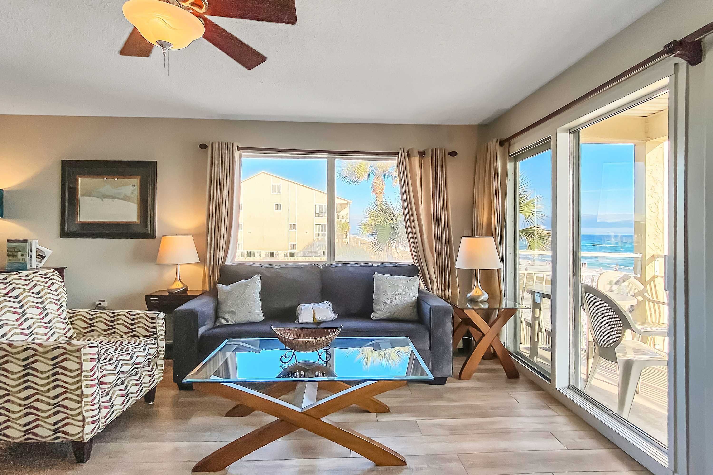 A modern living room with a sofa, a glass coffee table, and a ceiling fan.