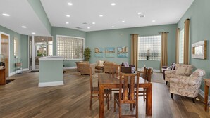 Un salón amplio con zona de comedor, que presenta suelo de madera, paredes verde claro y diversas opciones de asientos.