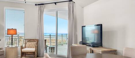 A hotel room with a balcony, a television, a dining table, and a chair.
