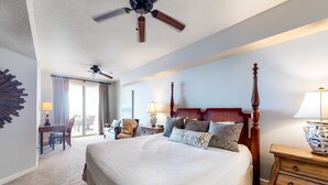 Habitación de hotel con una cama grande, ventilador de techo, escritorio con silla y vistas al exterior.