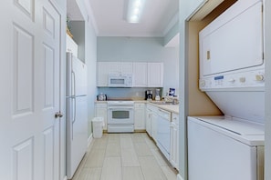 A compact kitchen with white cabinets, a microwave, an oven, a dishwasher, and a washing machine. - Inviting Gulf-front condo In Perdido Key with waterfront pool/hot tub and oceanfront balcony (Perdido Key)