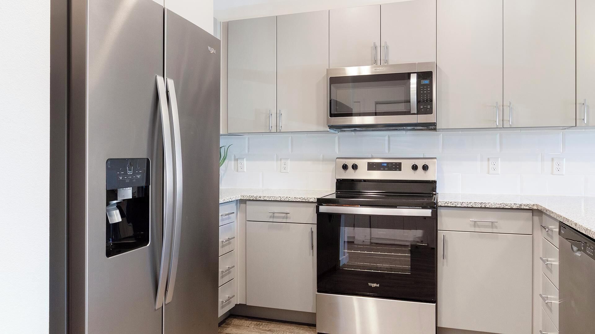 A modern kitchen with stainless steel appliances, including a refrigerator, microwave, oven, and dishwasher.