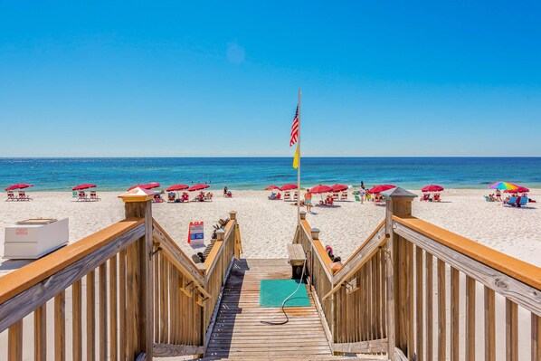 Een houten looppad dat naar een strand leidt, met parasols en strandstoelen.