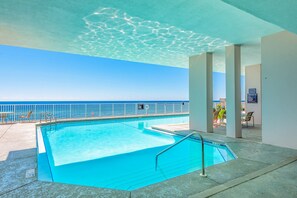 Een binnenzwembad met helderblauw water, uitzicht op de oceaan en een witte balustrade.