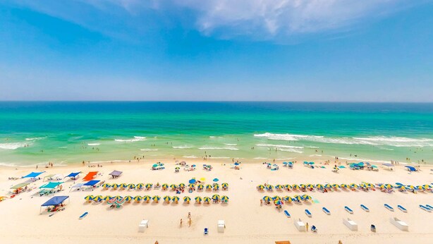 Una spiaggia con file di lettini e ombrelloni, cielo sereno e mare.