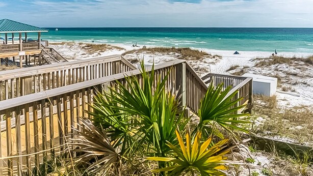 A beach with a wooden boardwalk, a beach hut, and a view of the ocean. - Family-friendly Gulf view condo with beach chair & umbrella, shared pool,hot tub (Miramar Beach)