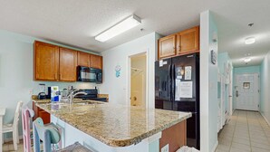 A kitchen with granite countertops, wooden cabinets, a refrigerator, and a microwave. - Family-friendly Gulf view condo with beach chair & umbrella, shared pool,hot tub (Miramar Beach)