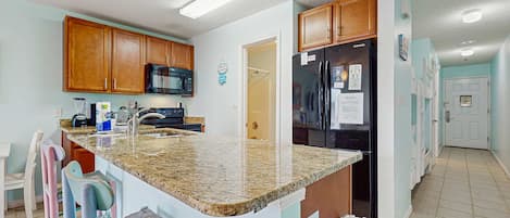 A kitchen with granite countertops, wooden cabinets, a refrigerator, and a microwave.