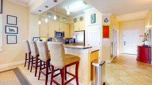 A kitchen with a central island, wooden chairs, a microwave, and a refrigerator. - Inviting Gulf-front condo In Perdido Key with waterfront pool/hot tub and oceanfront balcony (Perdido Key)