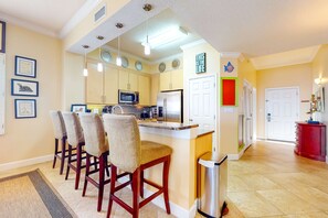A kitchen with a central island, wooden chairs, a microwave, and a refrigerator. - Inviting Gulf-front condo In Perdido Key with waterfront pool/hot tub and oceanfront balcony (Perdido Key)