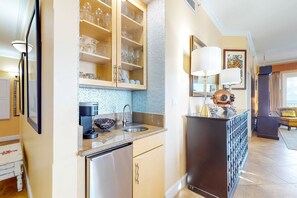 A modern kitchen with a built-in dishwasher, a sink, and a coffee machine. There is a cabinet with glassware and a decorative lamp. - Inviting Gulf-front condo In Perdido Key with waterfront pool/hot tub and oceanfront balcony (Perdido Key)