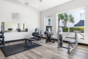A modern gym with various exercise equipment, large windows, and a view of palm trees. - Gorgeous 3-bedroom condo with stunning view, spacious balcony & pickleball (Santa Rosa Beach)