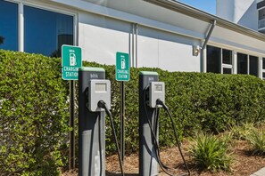 Two Blink EV charging stations with signs, in front of a building with a white exterior and a green hedge. - Gorgeous 3-bedroom condo with stunning view, spacious balcony & pickleball (Santa Rosa Beach)