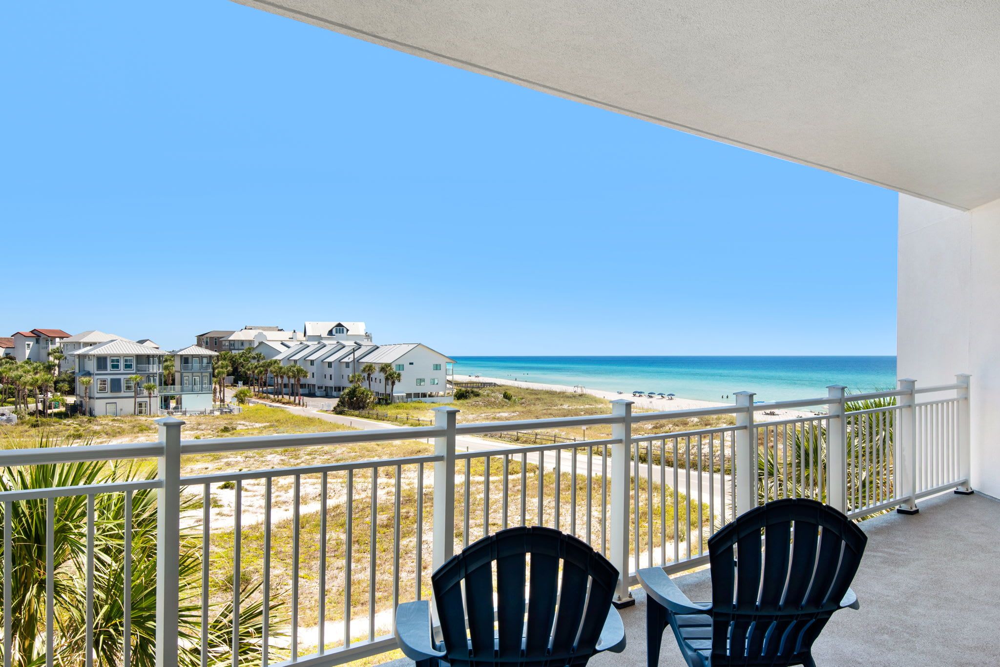 A balcony with two chairs overlooking a beach and ocean.