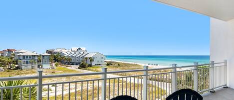 A balcony with two chairs overlooking a beach and ocean.