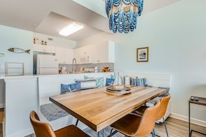 A modern kitchen with white cabinets, a wooden dining table, and a hanging blue chandelier. - Comfortable Gulf-front condo with beach chairs - near dining (Fort Walton Beach)