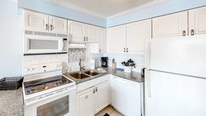 Une cuisine moderne avec des meubles blancs, un four à micro-ondes, une cuisinière, un évier et un lave-vaisselle.