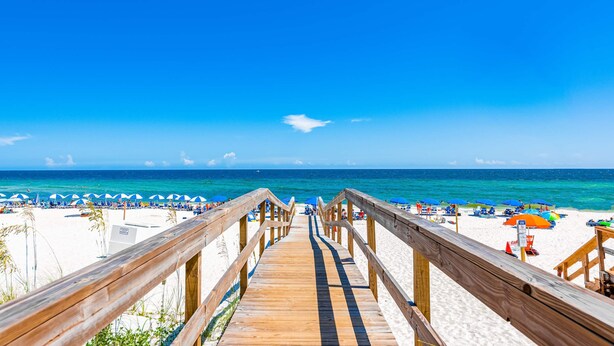 Une promenade en bois menant à une plage où l’on trouve des parasols et des chaises de plage.