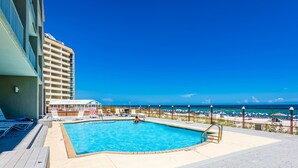 Un espace piscine offrant une vue sur la plage et l’océan, agrémenté de chaises longues et de parasols.