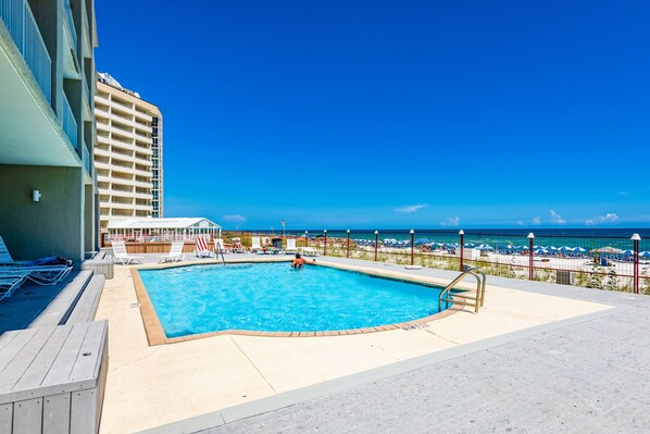 A pool area with a view of the beach and ocean, surrounded by lounge chairs and umbrellas. - Oceanfront Condo with Shared Pool, Ocean View, WiFi, Central AC, and Private W/D (Perdido Key)