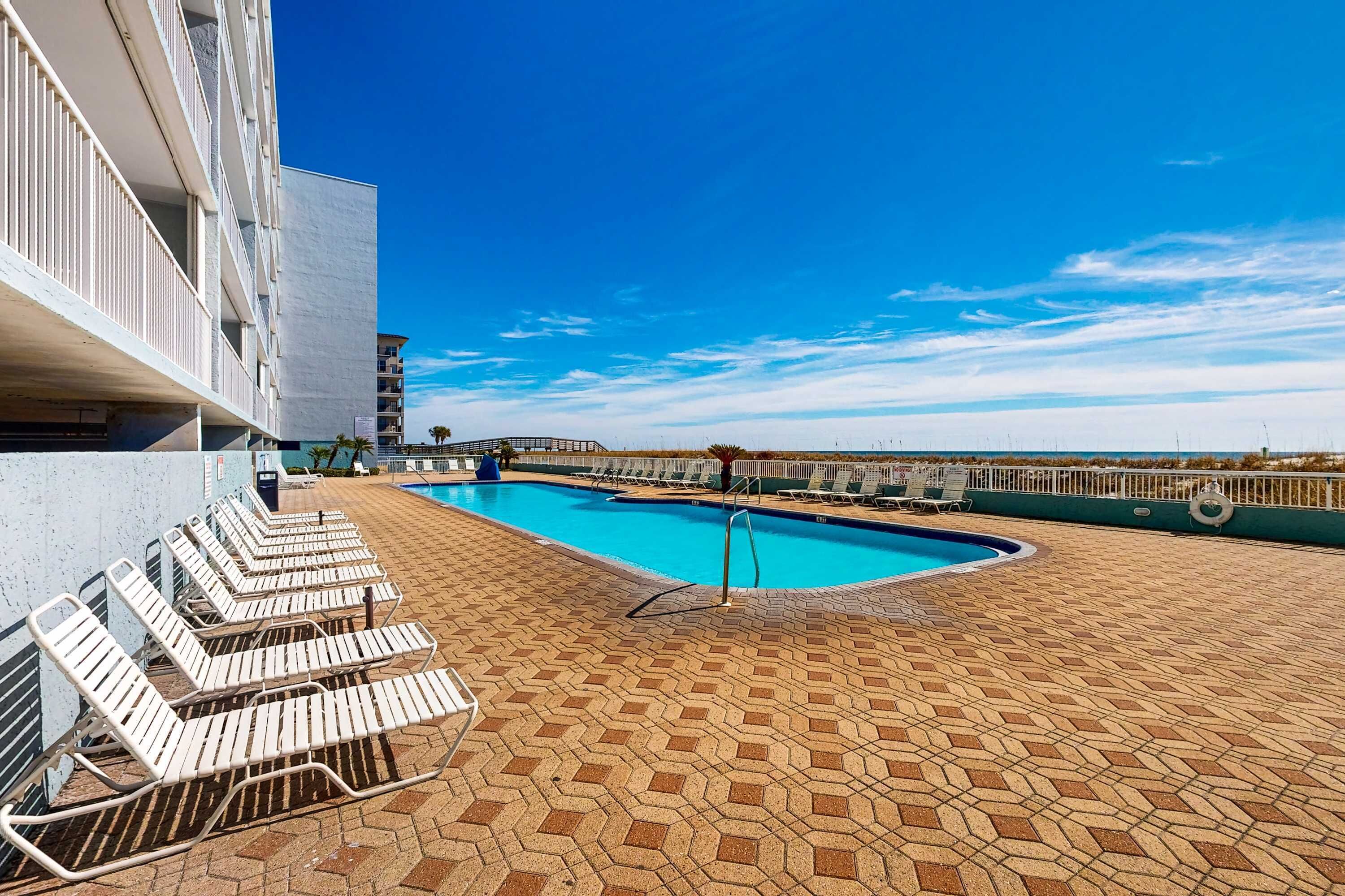 Una piscina con lettini, un cielo azzurro limpido e un edificio sullo sfondo.