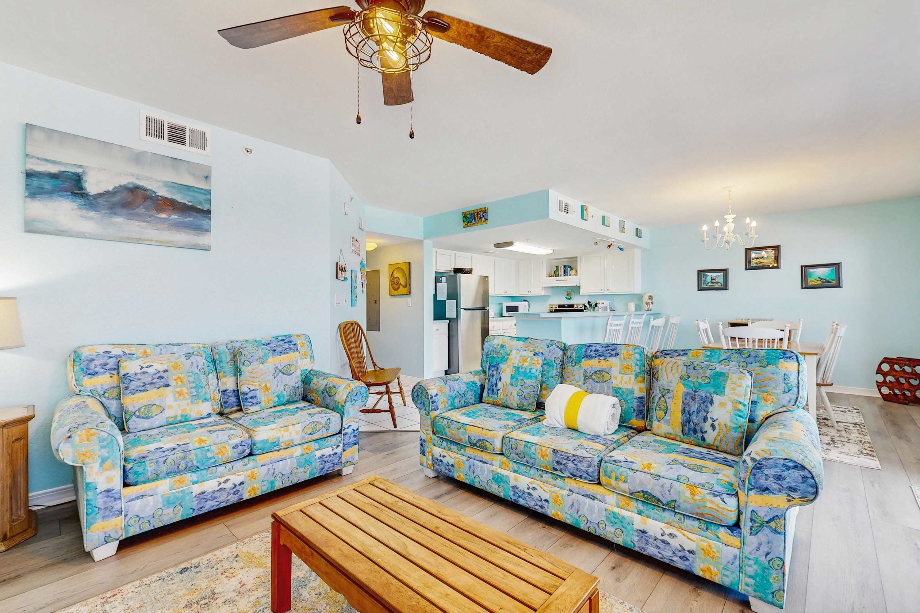 A living room with two patterned sofas, a wooden coffee table, and a ceiling fan.