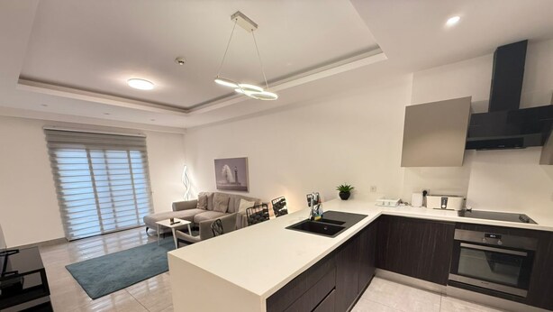 A modern kitchen with a central island, dark cabinetry, and a built-in oven. - Sky Suites Mirage (Accra)