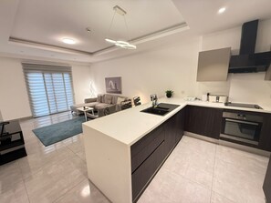 A modern kitchen with a central island, dark cabinetry, and a built-in oven. - Sky Suites Mirage (Accra)