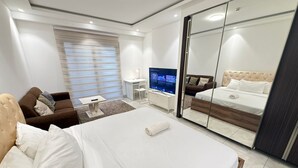A modern hotel room with a large bed, a sofa, a TV, and a sliding door closet. - Sky Suites Mirage (Accra)