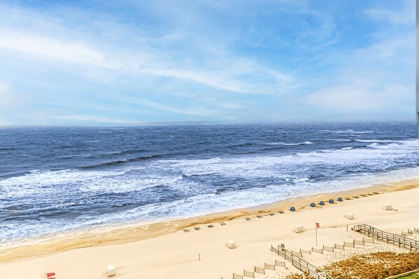 Une plage avec un rivage sablonneux, une rangée de chaises longues bleues et un mât de drapeau.