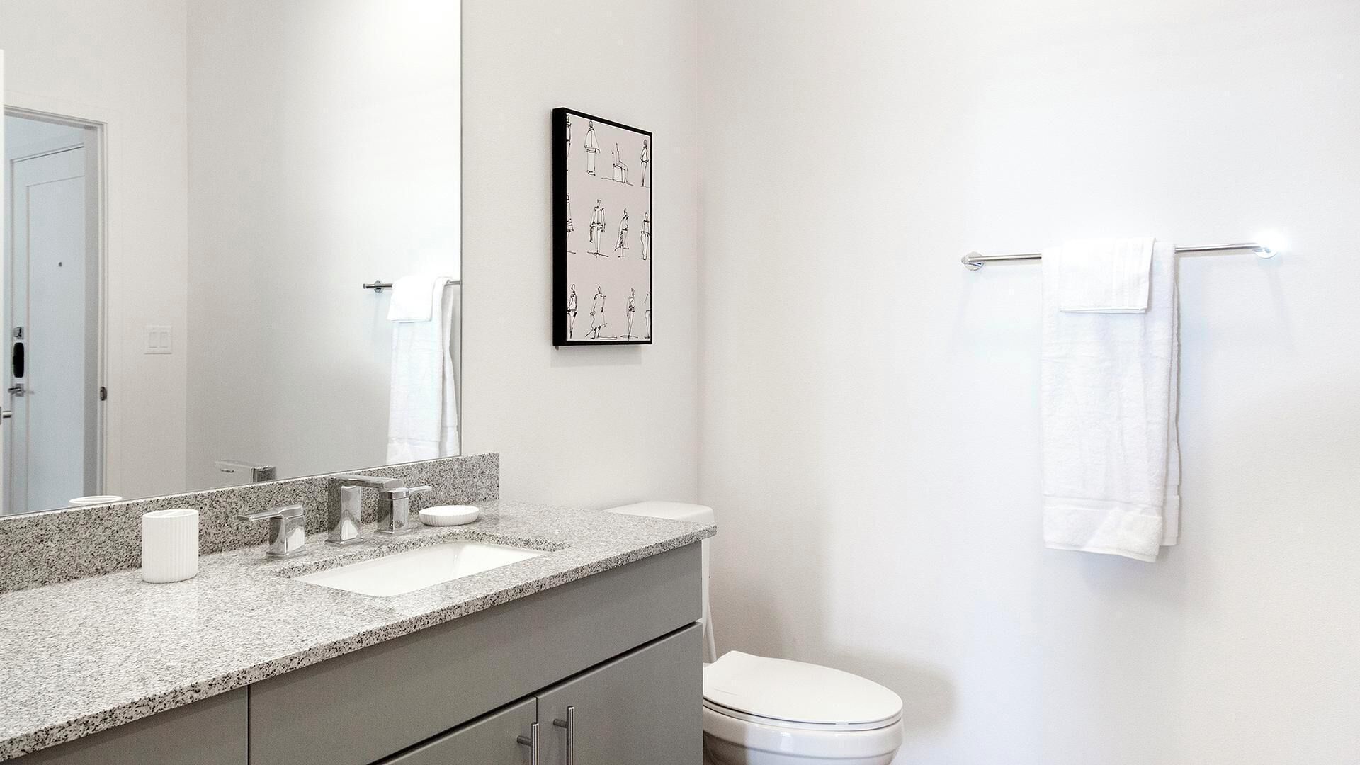 A modern bathroom with a granite countertop, two sinks, a toilet, and a towel rack.