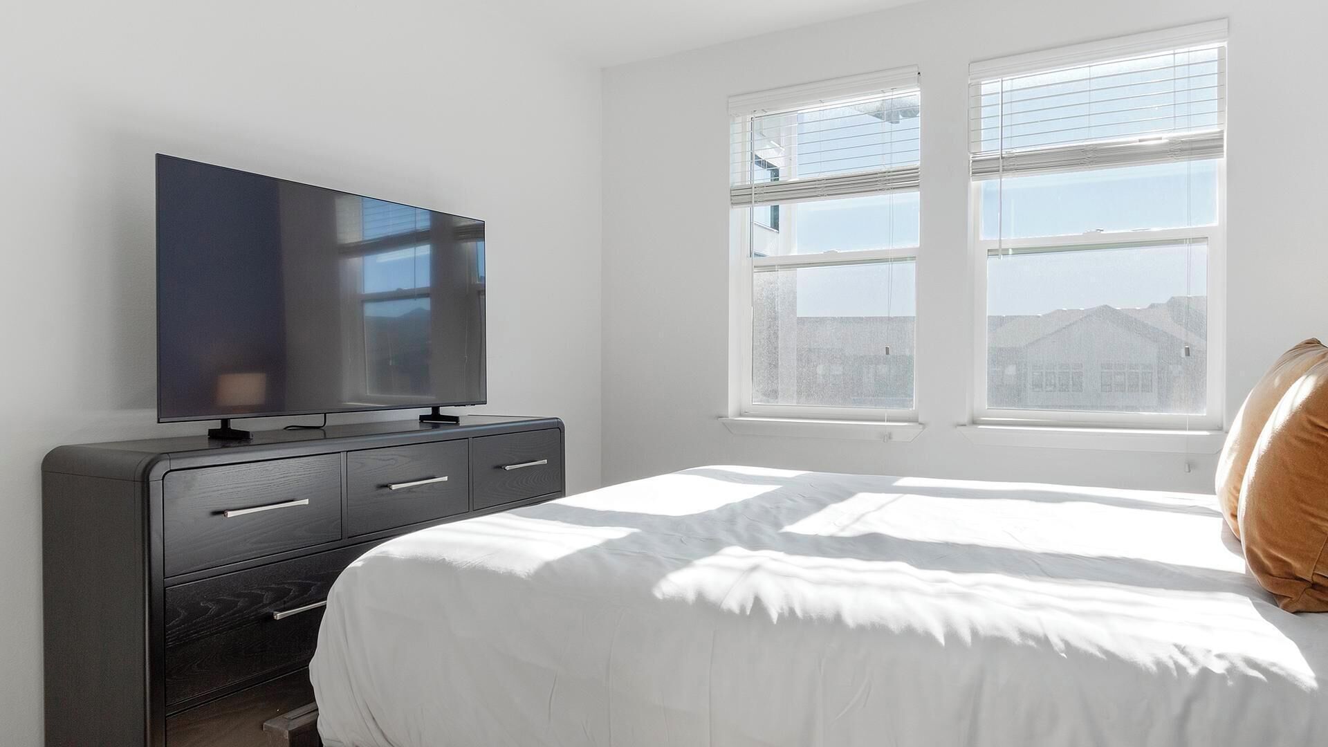 A bedroom with a bed, a TV on a dresser, and a window with a view.