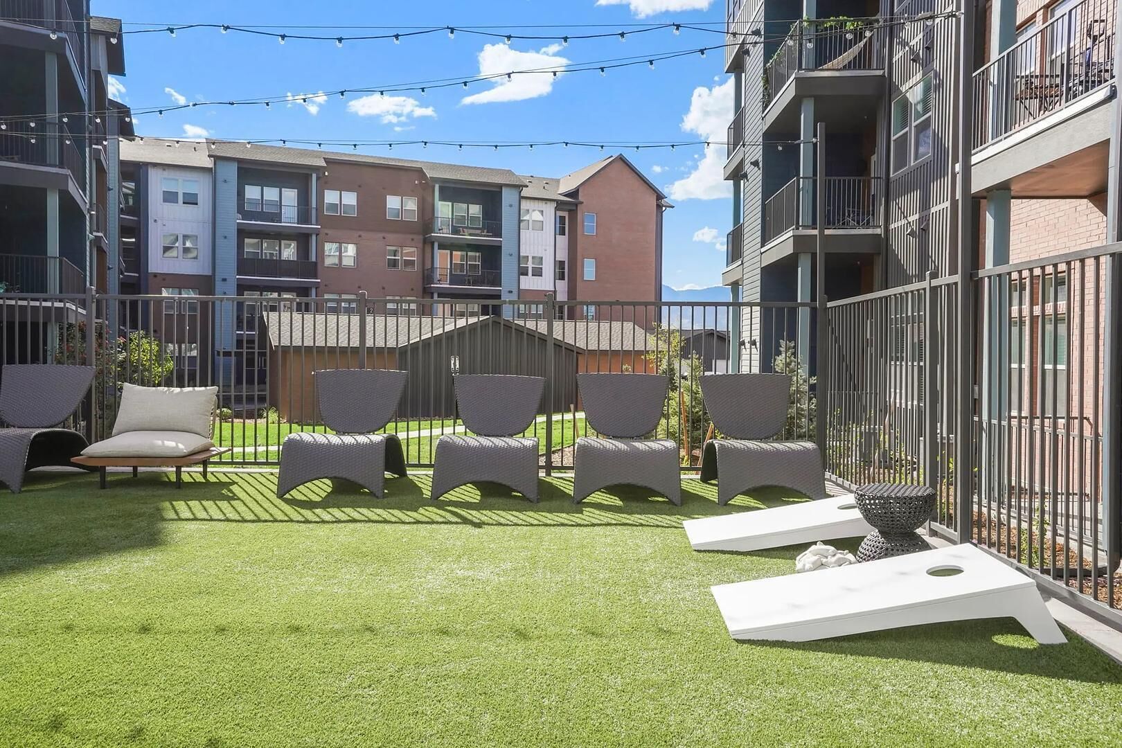 A courtyard with artificial grass, outdoor seating, and a metal fence.