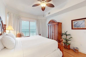 A bedroom with a large bed, a ceiling fan, a view of the ocean through a window, and a wooden cabinet. - Inviting Gulf-front condo In Perdido Key with waterfront pool/hot tub and oceanfront balcony (Perdido Key)