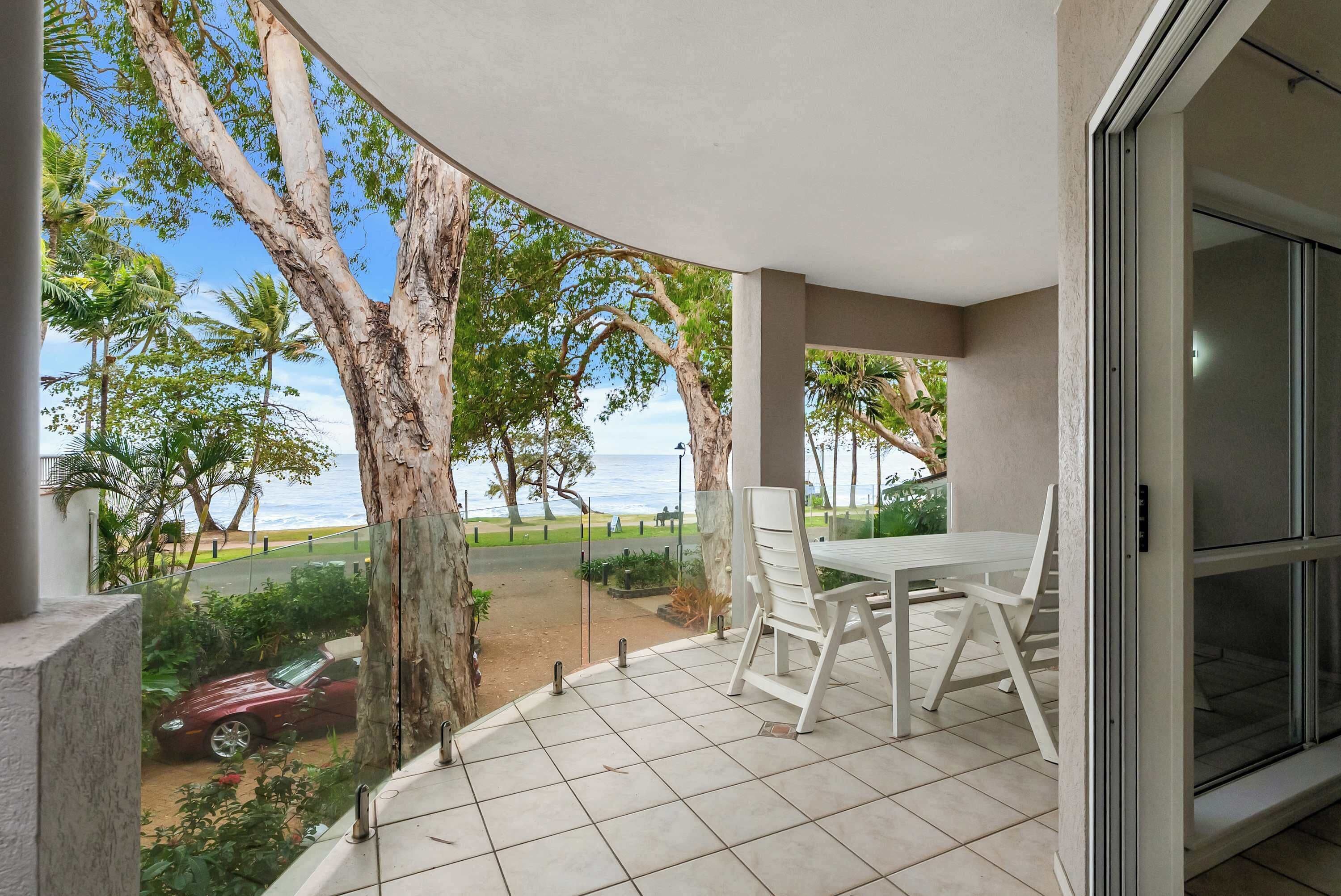 A balcony with a white table and chairs, overlooking a beach and trees.