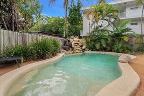 A swimming pool with a stone wall and tropical vegetation. - Yasmin at Coral Horizons: Retro Vibes on the Beach (Palm Cove)