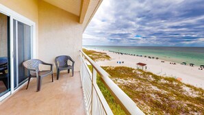 Ein Balkon mit zwei Stühlen, der auf einen Strand mit Sonnenschirmen und einem Sandbereich blickt.