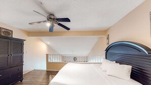 Ein Schlafzimmer mit Bett, Deckenventilator, dunklem Kopfteil und Holzboden.