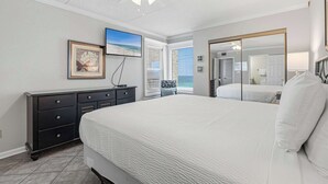 Ein Schlafzimmer mit einem großen Bett, einem Deckenventilator, einem Schminktisch, einem gerahmten Bild und einem Fenster mit Jalousien.