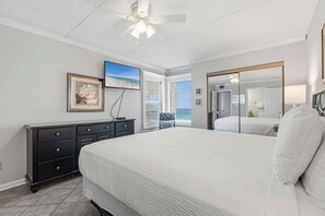 Ein Schlafzimmer mit einem großen Bett, einem Deckenventilator, einem Schminktisch, einem gerahmten Bild und einem Fenster mit Jalousien.
