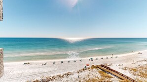 Ein Strand mit blauem Himmel, sandigem Ufer und einer hölzernen Promenade, die zum Strand führt.