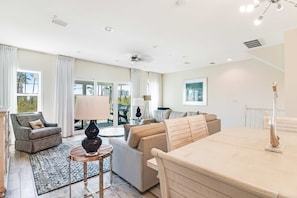 A spacious living room with a sofa, armchair, and a dining table. - Dog-friendly townhouse with two pools, hot tub, easy beach access, bikes, & deck (Perdido Key)